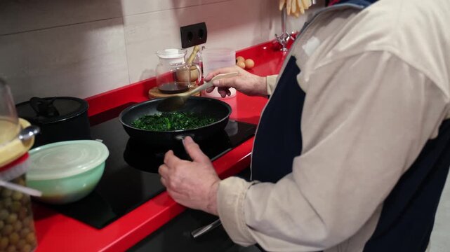 Male cook stirring spinach with a wooden spoon in a pan on an induction hob