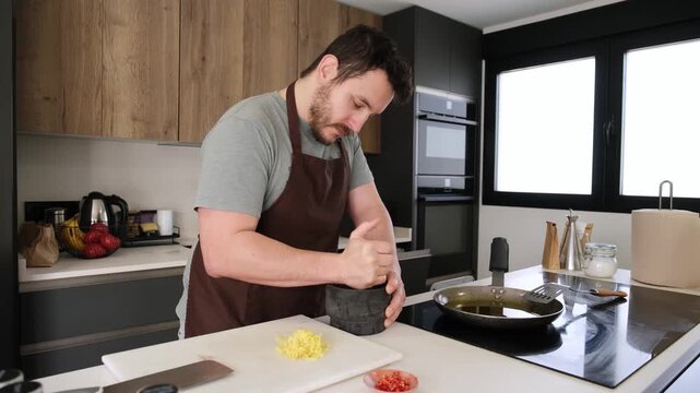 Concentrated man grinding ingredients in a mortar to prepare an aromatic sauce for a recipe at home