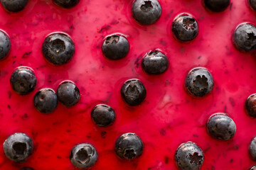 Detailed macro shot of juicy blueberries embedded in a vibrant pinkish-red jelly topping. The textured berry background creates a bright and delicious visual effect. © Олег Струс