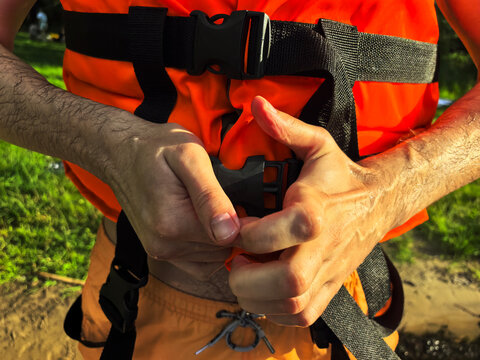 Man fastening orange life jacket buckle with both hands outdoors, water safety and personal flotation device preparation concept
