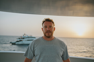 Fototapeta premium Man standing on a yacht deck, watching a golden sunset over the ocean