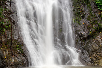Obraz premium White water cascading over dark mossy rocks in a lush tropical forest waterfall.