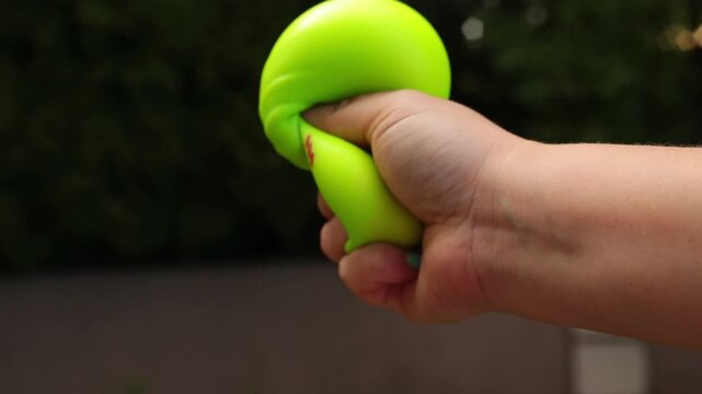 A hand squeezes a cute bright lime-green dumpling stress toy with small ears and a kawaii face, set against a dark blurred background