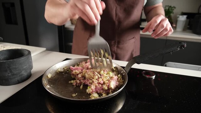 Male chef frying minced meat and chopped onions in a frying pan on an induction stove