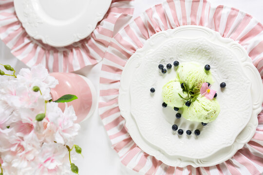A serving of pistachio-mint ice cream with blueberries on a white plate with floral decorations in pink pastel colors
