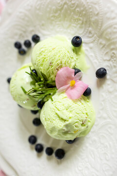 A serving of pistachio-mint ice cream with blueberries on a white plate with floral decorations in pink pastel colors