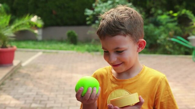 A boy holds a bright lime-green dumpling toy in his hands, squeezing its soft squishy surface while standing outdoors in natural daylight