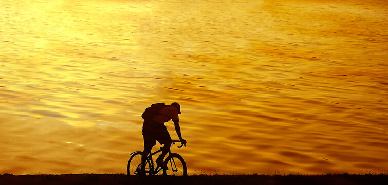 Silhouette of one  man guy boy ride a bicycle on sunset sea water background Male cyclist backpacker bicyclist rides with backpack rucksack along horizon line against sunrise heaven Healthy lifestyle