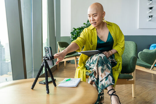 Woman Sits at Table and Records Video With Phone on Tripod