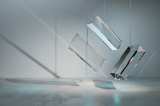 Three rectangular glass prisms hanging from thin wires in a bright room casting colorful light refractions on the floor and walls