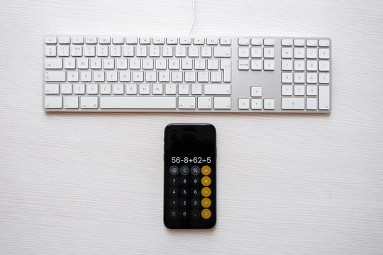 A computer keyboard and a calculator in a smartphone lie side by side on the desktop in the office.
