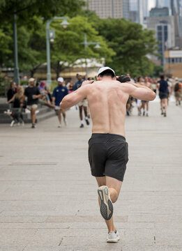 Shirtless Male Runner Exercising on Busy Urban Waterfront Promenade