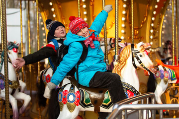 Schoolchildren with backpacks in winter clothes enjoy a ride on a carousel with colorful horses and bright lights © Светлана Лазаренко