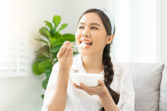 Healthy lifestyle, wellness food asian young woman hand use spoon eat tasty fresh organic yogurt, dairy product in bowl breakfast meal at home. Snack tasty on diet nutrition delicious natural yoghurt