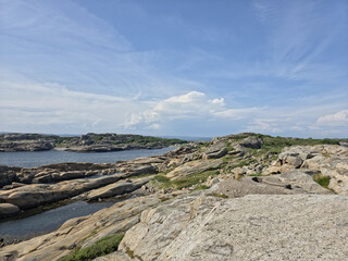 Rocky coastal landscape with calm sea, dramatic blue sky and layered clouds. Natural shoreline scenery with copy space, ideal for travel, nature and outdoor themes. © GlaDDeN