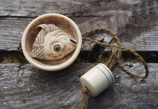 Japanese netsuke fish head in a ribbed bowl, wooden background, traditional art piece with history