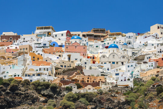 Colorful hillside view of Santorini&rsquo;s iconic whitewashed houses and blue‑domed churches under a clear blue sky, capturing the island&rsquo;s vibrant Mediterranean charm.
