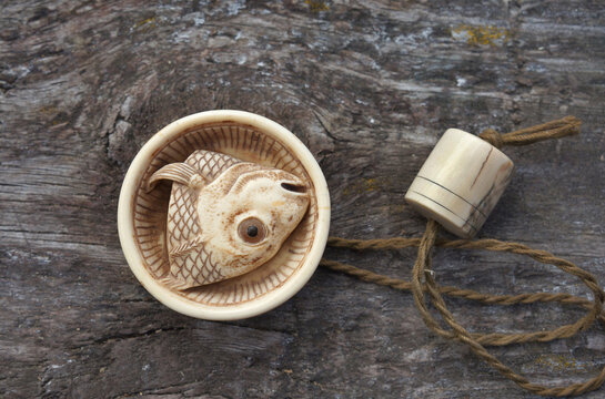 Japanese netsuke fish head in ribbed bowl on wooden background
