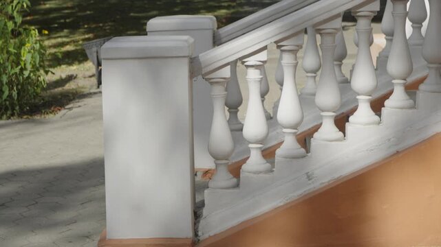 A classic white stone balustrade features sculpted balusters lining an outdoor staircase next to a paved walkway and green park background.