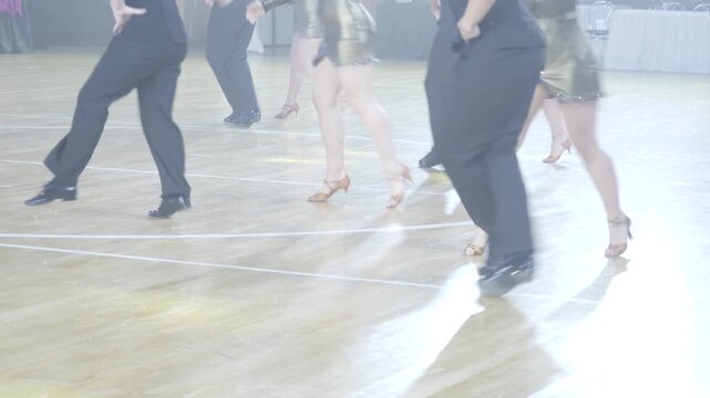 Professional ballroom dancers perform a synchronized Latin routine on a wooden dance floor in a lit venue.