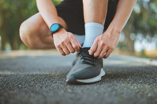 Close up of an Asian fitness man tying sneaker shoelaces while crouching down on an outdoor park path before morning exercise. Healthy active lifestyle, running preparation, wellness