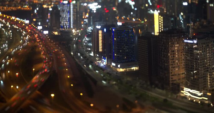 Dubai at night, dense car light trails fill the multi lane highway, lit residential towers stand along the road, tilt shift lens creates a miniature model look, timelapse