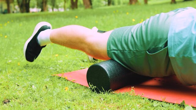 Man doing foam rolling on a mat outdoors in a park for myofascial release, self-massage, and post-workout muscle tension recovery. High quality 4k footage