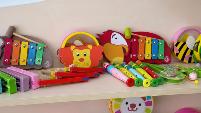 A camera pans across a wooden shelf neatly arranged with colorful children musical instruments including xylophones, tambourines, flutes, and castanets in a preschool room.