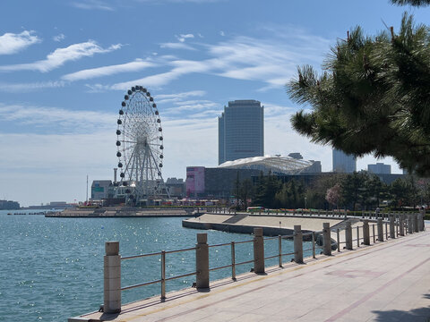 Qingdao, Shandong, China - April 20, 2026: Sunlit waterfront promenade overlooks turquoise harbor with metal railing in foreground