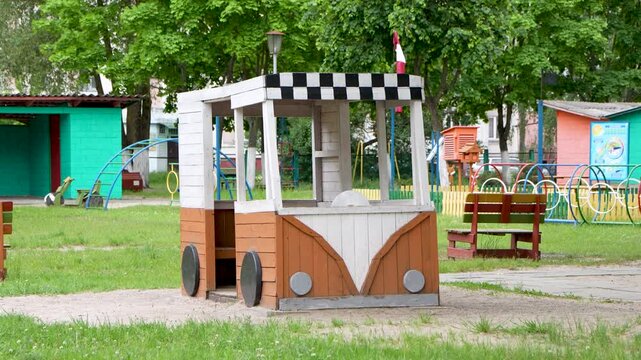 A handcrafted wooden play car stands in the center of a green public playground park on a overcast day.