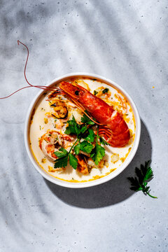 Creamy seafood chowder soup with big prawn, mussels in bowl on grey table. Vertical orientation gourmet seafood banner background, premium restaurant meal concept.