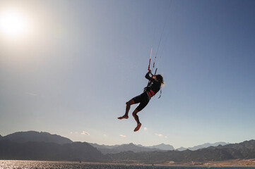 Kitesurfer wykonujący skok nad morzem na tle gór podczas słonecznego dnia © siwyk