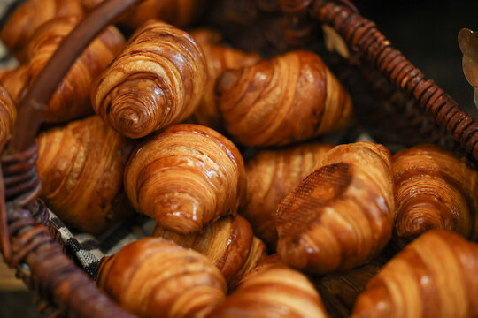 Fresh golden-brown croissants stacked in a wicker basket, showcasing flaky pastry layers and buttery texture in a bakery or caf&eacute; setting.