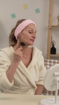 A woman in a bathrobe sits on a sofa enjoying her skincare routine, creating a relaxing atmosphere at home during her evening rituals. She uses a Nerf facial roller massager.