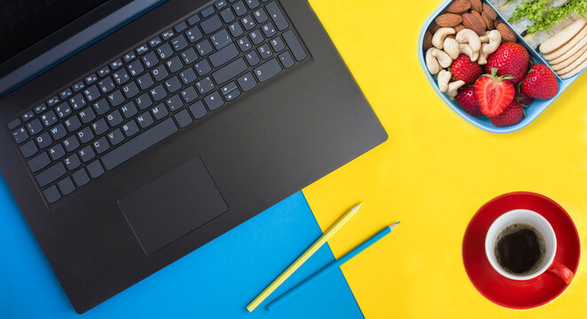 Office desk with laptop, pencils, coffee cup and lunch box on a colored background. Workspace desk. Top view.
