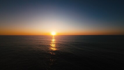 Obraz premium Aerial view of sun dipping into ocean, calm waters shimmering with golden light