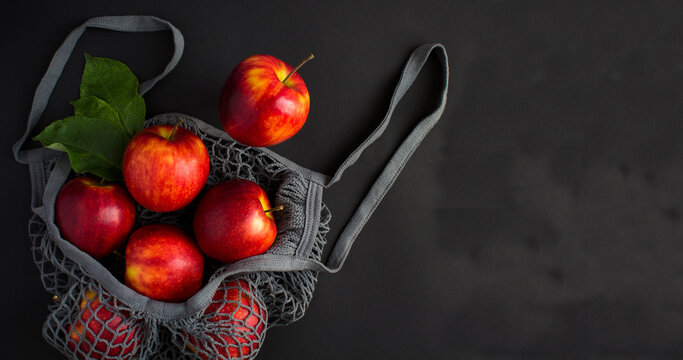 Mesh shopping gray bag with red apples on a black background. Top view. Copy space.