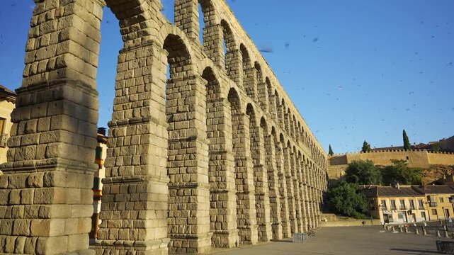 Wide angle view of the Roman Aqueduct of Segovia stretching across the historic plaza under blue sky