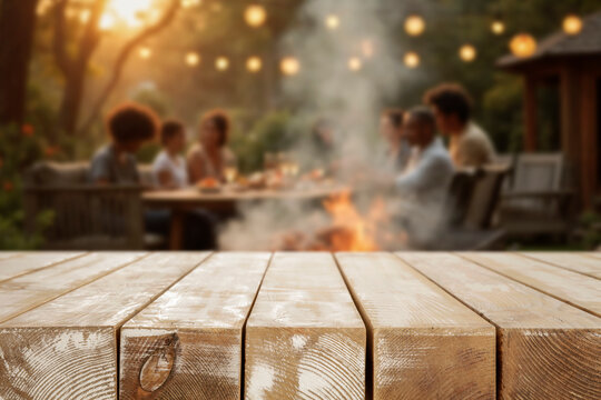 Empty wooden table for product placement. Blurred background with friends and family gathered in garden enjoying summer barbecue on sunny day. 