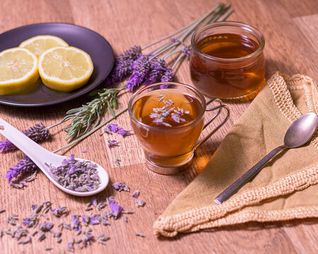 A warm cup of lavender tea served with honey, lemon slices, dried lavender buds, and a spoon on a rustic wooden table in soft lighting