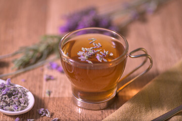 Fototapeta premium A warm cup of lavender tea served with honey, lemon slices, dried lavender buds, and a spoon on a rustic wooden table in soft lighting