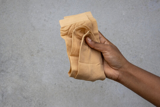 Close-up female hand holding a pair of folded skin color socks. Premium stretchable nylon thin hosiery for women lifestyle clothing. Comfortable breathable elastic cotton texture.
