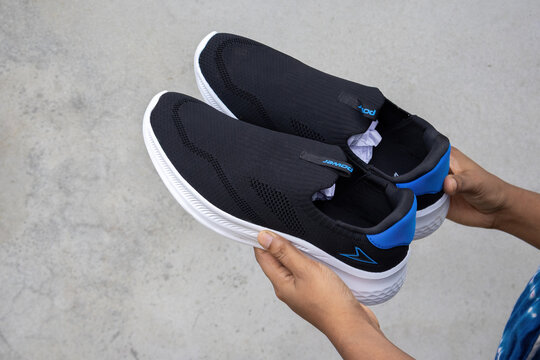 Close-up female hand holding pair of new black slip on sports shoes. Modern athletic running sneakers with white sole and blue details. Comfortable active lifestyle gear.