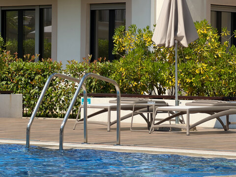 Swimming pool with empty sun loungers under bright sunlight at a hotel, peaceful summer vacation and luxury resort concept