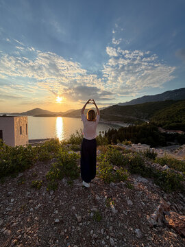 Woman standing on high rocky Adriatic Sea coast illuminated by golden sunset light, dramatic Mediterranean landscape and travel freedom conceptconcept