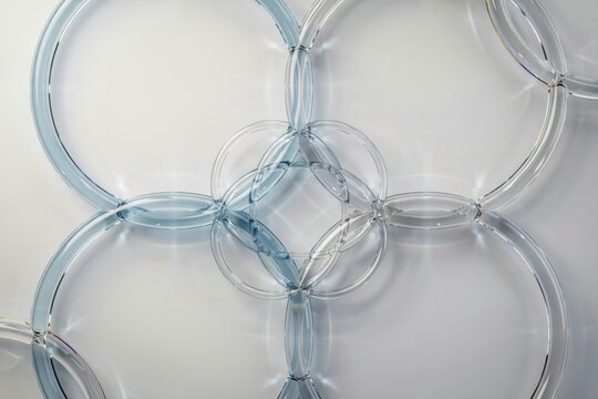 Abstract composition of interconnected transparent glass rings creating a geometric pattern on a clean white background, with soft light reflections