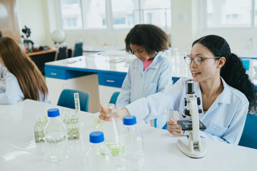 Fototapeta premium Laboratory scientist women in white coat using microscope during chemistry experiment in bright classroom
