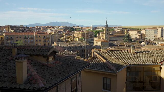 Panoramic view across the historic rooftops of Segovia with church tower and distant mountains under a clear blue sky