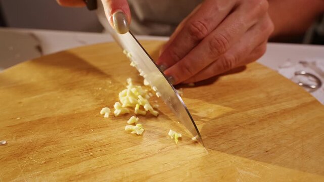 Close View of Female Hands Finely Chopping Fresh Garlic on Wooden Kitchen Board, Aromatic Seasoning and Homemade Food Preparation