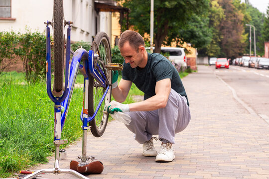 Man examining bike chain and gears for wear. Upside down position reveals issues. Practical competence outside house